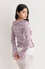 Top de manga larga color celeste/turquesa, confeccionado en tejido de encaje floral. Presenta escote en V con volados en el borde y lazos ajustables en el centro del escote y en los puños.