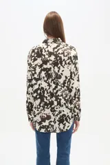 Camisa holgada de manga larga, color negro, con cuello camisa y botones frontales. Presenta apliques de tachas plateadas en los hombros y a lo largo de la tapeta frontal.