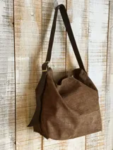 Bolso marrón de cuero con textura, tipo hobo, con correa larga regulable y hebilla dorada.