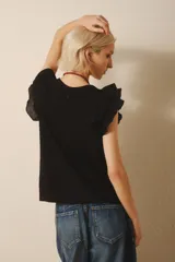Remera negra sin mangas con volados en los hombros y escote en V. Incluye un collar largo de cuentas con un nudo decorativo. Jeans de tiro bajo.