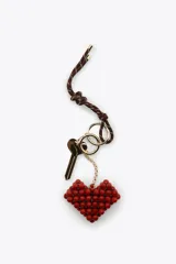 Llavero con cordón marrón y blanco, llave dorada y dije colgante de corazón rojo hecho con cuentas. Incluye aros metálicos dorados.