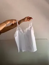 Top blanco con breteles finos y detalles de encaje en el escote y ruedo.