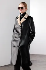 Abrigo largo de Zara Woman Collection, confeccionado en tejido efecto piel color negro. Tiene cuello solapa, manga larga, bolsillos laterales ocultos y forro interior de borreguillo color beige. El cierre es cruzado con botones.
