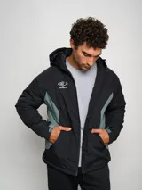 Campera corta de abrigo Umbro Crafted Pro, color negro con paneles laterales en gris. Presenta capucha con cordón ajustable, cierre frontal completo y logo de la marca bordado en el pecho.