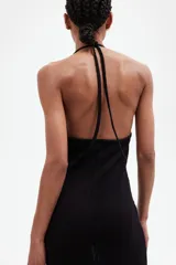 Vestido largo de punto pointelle negro con estilo crochet. Modelo entallado con escote halter en V y adorno de metal en forma de sol en el centro del busto. Falda sirena con bajo recto.
