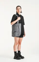 Bolso tipo tote bag color gris, confeccionado en microfibra técnica de secado rápido. Cuenta con un compartimento principal con elástico ajustable, un bolsillo interno con cierre y un bolsillo externo con velcro.