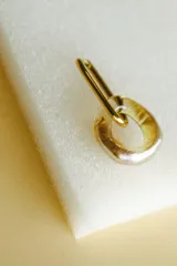 Aros colgantes con forma de eslabón, con un eslabón de metal dorado y otro de vidrio transparente con reflejos dorados.
