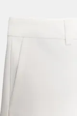 Short blanco de tiro bajo, corte ajustado y largo mini. Presenta bolsillos delanteros y cierre frontal con cremallera y gancho metálico.