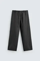 Pantalón negro de corte relajado y pierna ancha, confeccionado en mezcla de algodón y lino. Presenta cintura elástica ajustable con cordón y cierre frontal con cremallera y botón.