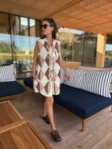 Vestido camisero corto con estampado de rombos en tonos beige, marrón y blanco. Tiene cuello camisero, cierre frontal con botones y corte holgado.