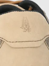 Zapatilla acordonada de cuero color beige con perforaciones en los laterales y suela blanca con base de goma color caramelo.