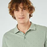 Chomba de piqué de algodón color verde claro con estampado de pequeñas figuras geométricas en negro. Tiene cuello clásico con botones y mangas cortas.