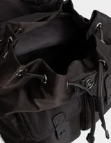 Mochila de tela color lila, con solapa con broche y tira de ajuste, doble bolsillo frontal con broche y pouch con charm lateral en forma de cartera.
