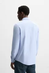 Camisa celeste a rayas verticales blancas, de corte recto, con cuello italiano abierto, manga larga con puños abotonados y cierre frontal con botones.