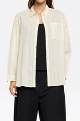 Camisa blanca con rayas verticales amarillas, de corte recto, manga larga con puños abotonados, cuello camisero y bolsillo de parche en el pecho.