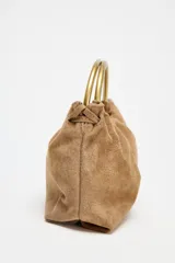 Bolso mini tipo saca de cuero serraje color marrón con efecto soft. Tiene doble asa de mano metálica dorada y asa bandolera extraíble. Cuenta con bolsillo interior con cremallera y cierre mediante fruncido y botón imantado.