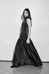 Vestido largo negro con finas líneas plateadas, de corte holgado, escote halter y espalda baja. Presenta volados en el cuello y en la cadera.