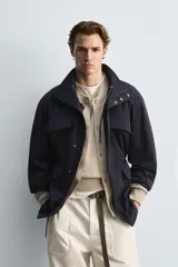 Parka azul marino de tejido técnico, corte relaxed fit, cuello alto ajustable con cordón, manga larga con puños abotonados, cierre frontal con cremallera oculta y solapa con botones a presión, cintura ajustable con cordón interior y bolsillos frontales multifunción de plastrón.