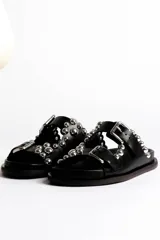 Sandalias marrones de cuero con dos tiras con hebillas ajustables y detalle de tachas plateadas.