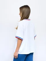 Remera blanca de corte clásico con cuello redondo y mangas cortas con puños tricolor (azul, blanco y rojo). Presenta el logo de Umbro bordado en el pecho izquierdo y el escudo del Club Nacional de Football bordado en el pecho derecho.