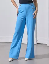 Pantalón largo de crepe elastizado color verde, de corte recto, con bolsillos delanteros y apliques de botones metálicos.