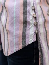 Camisa sin mangas de lino estampada a rayas verticales grises y blancas, con cuello camisero, cierre frontal con botones, dos bolsillos con solapa en el pecho y ruedo asimétrico con aberturas laterales.