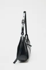 Bolso de hombro negro con asa ajustable mediante hebilla metálica. Tiene un bolsillo interior con cremallera y cierre principal también con cremallera.