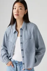 Camisa a rayas verticales azules y blancas, con cuello clásico, cierre frontal con botones y dos bolsillos de parche en el pecho.