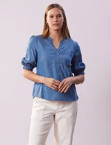 Blusa de lyocell color celeste, con cuello a la base, escote en V y botones. Delantera con bolsillo. Manga corta con terminación en punto smock.