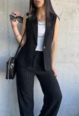 Chaleco negro con rayas verticales blancas, cuello en V y corte recto.