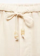 Pantalón crop de lino color crudo, de corte recto, con cintura elástica ajustable con cordón y bolsillos laterales.