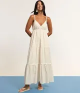 Vestido largo midi color crudo, con escote en V, breteles finos con detalles trenzados, lazo en la espalda, volados y adornos en el bajo.