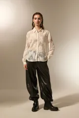 Camisa negra de poliamida con diseño calado de encaje floral, corte holgado, cuello camisero, botones frontales y mangas largas.