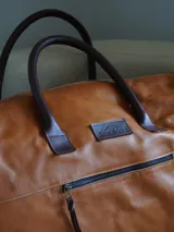 Bolso de viaje tipo weekender de cuero color marrón, con doble asa corta y correa larga desmontable. Cuenta con cierre superior, bolsillos internos y externos con cierre metálico. Forro interior de tela. Marca Sierra Mora.