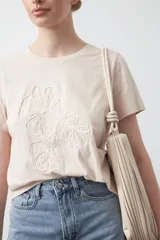 Remera blanca de manga corta con cuello redondo y bordado floral en relieve de color beige claro en el frente.