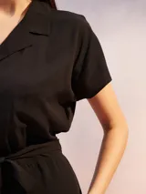 Mono corto negro de manga corta con cuello tipo solapa y cierre frontal de botones. Incluye un lazo de tela para ajustar a la cintura.