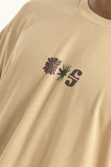 Remera color beige de corte holgado con estampado pequeño de palmera y la letra S en el centro del pecho.