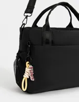 Cartera tipo tote de tela deportiva color negro, con correa regulable desmontable, manijas superiores, charm lateral con la palabra "Vibes", cierre superior, bolsillo frontal y bolsillos laterales de red.