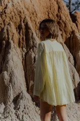 Camisa amarilla de algodón, corte suelto y largo asimétrico, más larga atrás que adelante. Tiene mangas largas amplias.