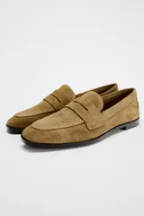 Zapato plano tipo mocasín color marrón claro, confeccionado en piel de serraje. Tiene copete subido, antifaz y punta redonda.