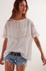 Remera blanca de algodón con cuello redondo y mangas cortas. Presenta detalles de encaje en el pecho y en las mangas.