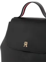 Mochila negra de poliuretano con forro de poliéster. Presenta un diseño estructurado con solapa superior que cierra con broche magnético y un asa de mano superior. En el centro de la solapa lleva un monograma metálico TH.