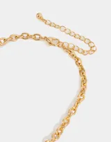 Collar corto dorado con cadena de eslabones gruesos y dijes colgantes: corazón, flor encapsulada, lazo, perla y cristales rosados.