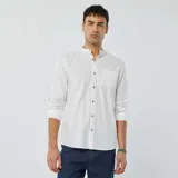 Camisa blanca de lino con cuello mao, manga larga con puños abotonados y bolsillo de parche en el pecho. Cierre frontal con botones a tono.