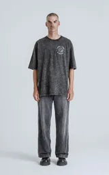 Remera negra con efecto nevado, de corte oversize y manga corta. Estampa circular en el pecho con la frase "Tarot Luxo El Mundo" y un dibujo del planeta Tierra.