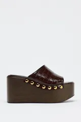 Mules de cuero marrón con plataforma de madera y detalle de tachas doradas.