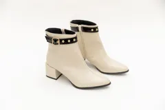 Botas de cuero negro, de caña baja, punta fina y taco cuadrado. Presentan un aplique charolado al tono, una correa con hebilla y ojales metálicos.