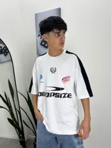 Remera blanca de corte holgado con mangas cortas negras y estampados con logos y texto en el frente.