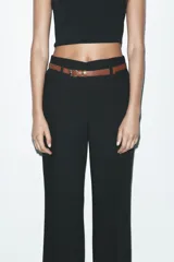 Pantalón marrón de tiro alto con cinturón negro, bolsillos delanteros y cierre frontal con cremallera y gancho metálico.