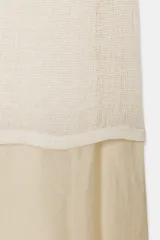 Vestido largo de punto ligero color crudo, con cuello redondo y mangas largas. Presenta un forro interior de tela satinada color beige claro que asoma en el bajo, creando un efecto de dos piezas.